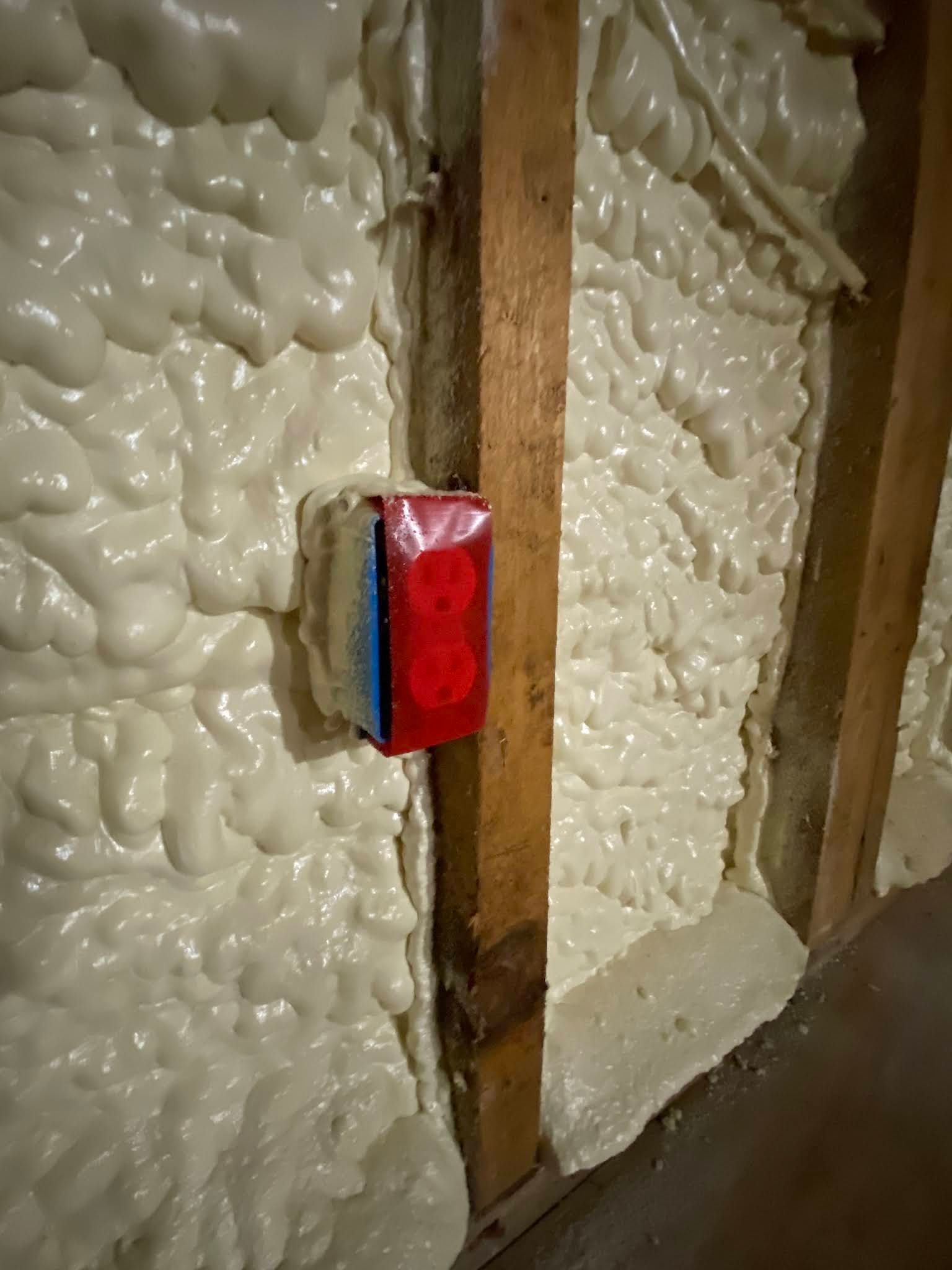 Spray foam insulated wall with exposed wooden studs and a red electrical box mounted on a stud