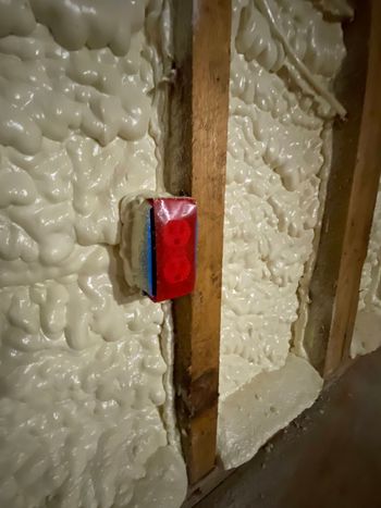 Foam-insulated wall with a red electrical box mounted on a wooden stud