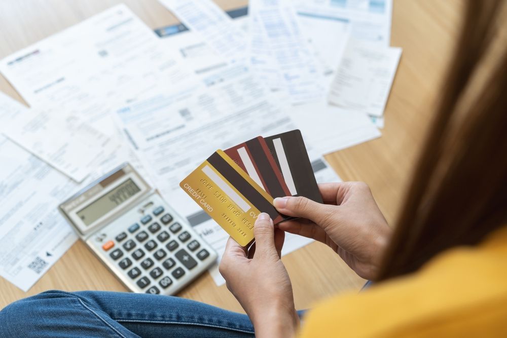 Person holding credit cards beside calculator and scattered bills on a desk