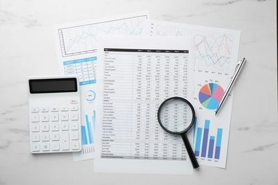 Calculator and magnifying glass on financial reports with charts and graphs on a white desk
