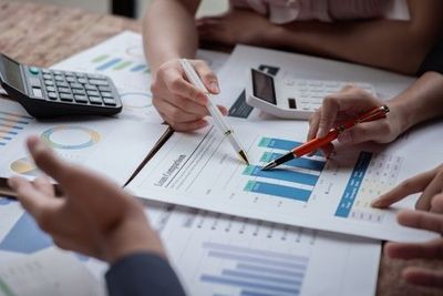 Hands pointing at business charts and graphs on a desk with a calculator and papers
