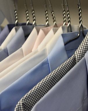 Neatly hung dress shirts in light blue, white, and patterned fabrics on metal hangers