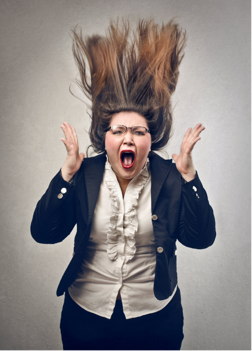 Woman in black blazer and white shirt screaming, hair flying upward against a plain gray background.