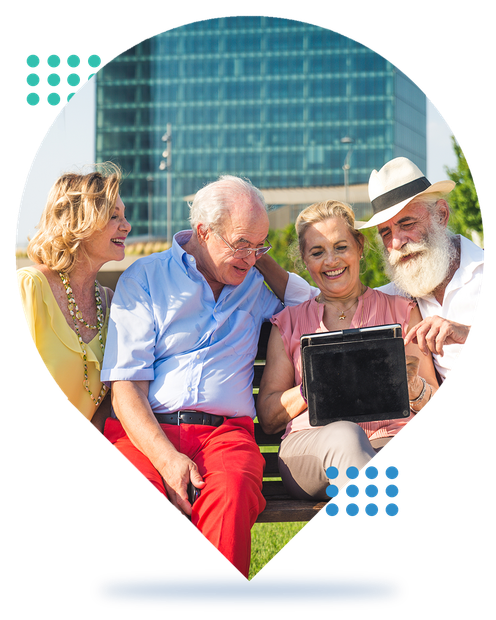 Four older adults smiling and looking at a tablet outdoors in a city park