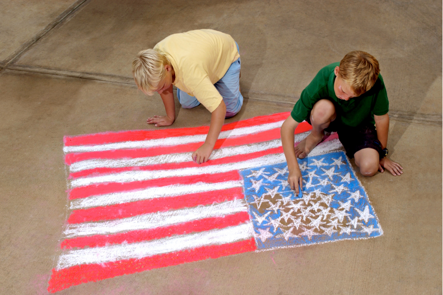 Two children painting a U.S. flag on a large paper sheet on the floor