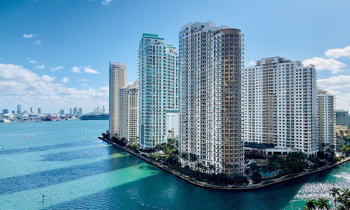 Waterfront high-rise condos on a peninsula, surrounded by turquoise water under a clear blue sky.