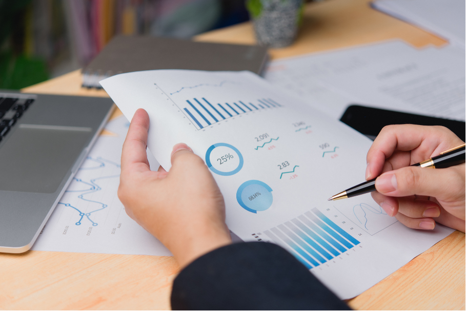 Hands reviewing printed charts and graphs at a desk with a laptop and pen