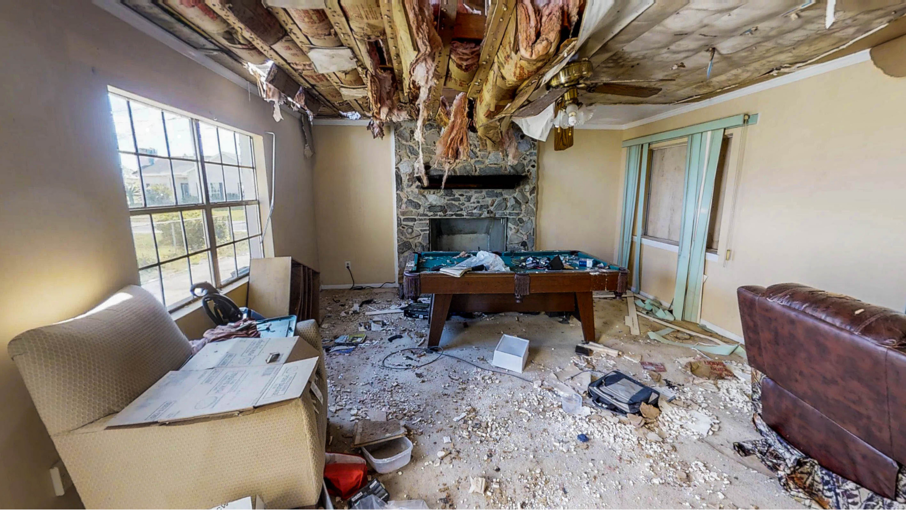 Dilapidated living room with collapsed ceiling, debris on floor, broken furniture, and damaged walls