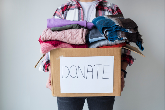 Person holding a box labeled “DONATE” with folded clothes on top