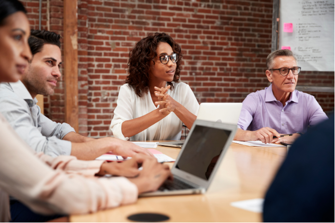 Team meeting in a brick-walled conference room, with people discussing around a laptop.