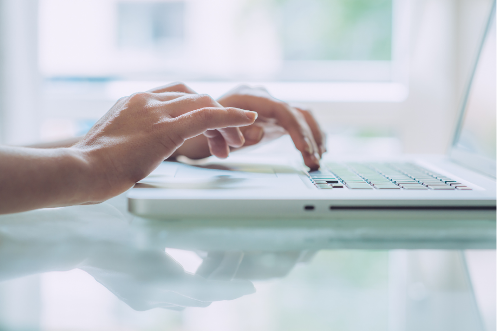 Hands typing on a white laptop in a bright room