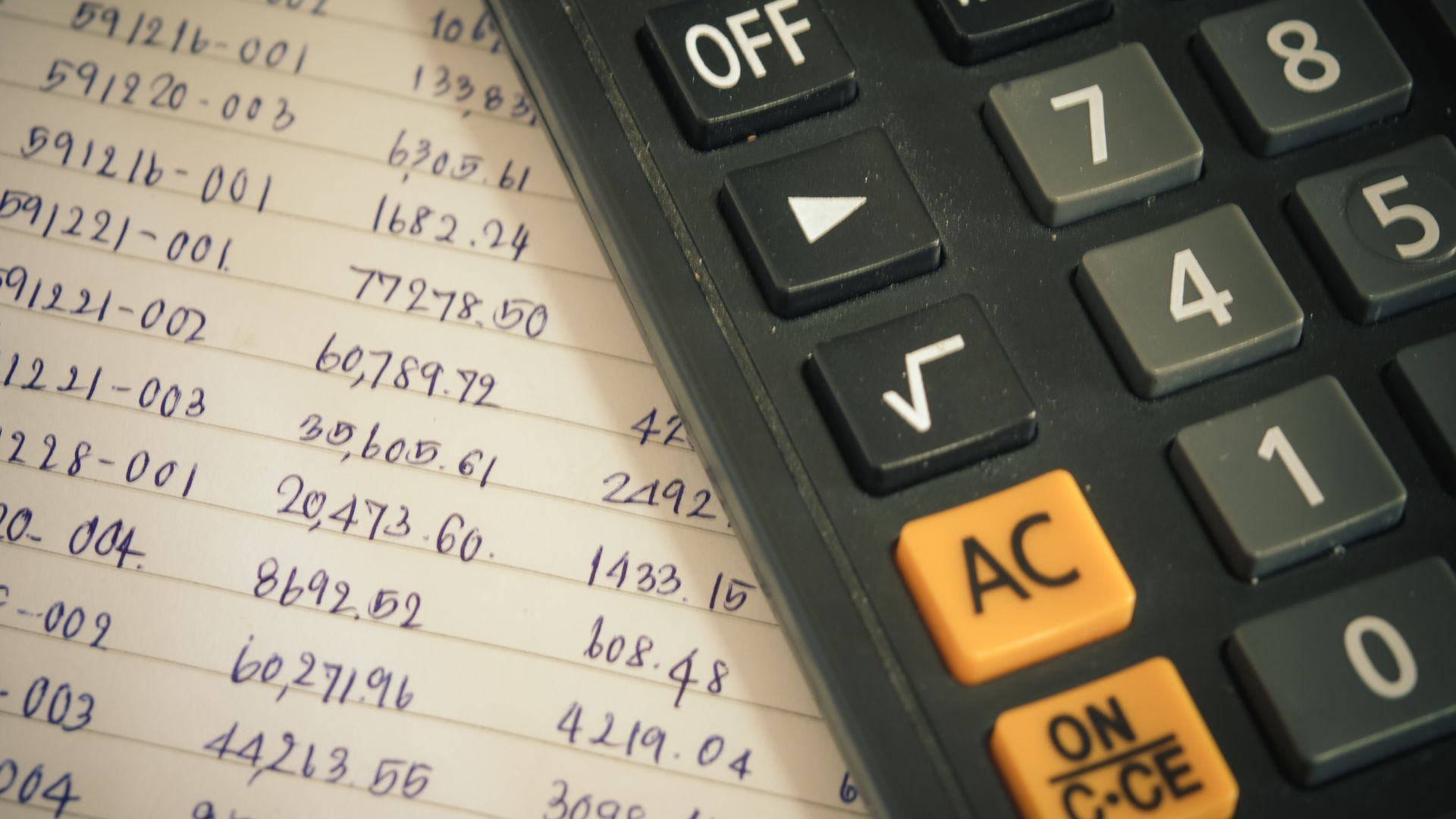 Calculator on financial paperwork with highlighted AC button and visible handwritten numbers