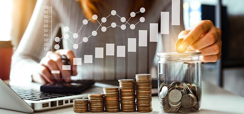 Laptop with rising bar chart, stacked coins, and a hand placing coins into a glass jar of savings