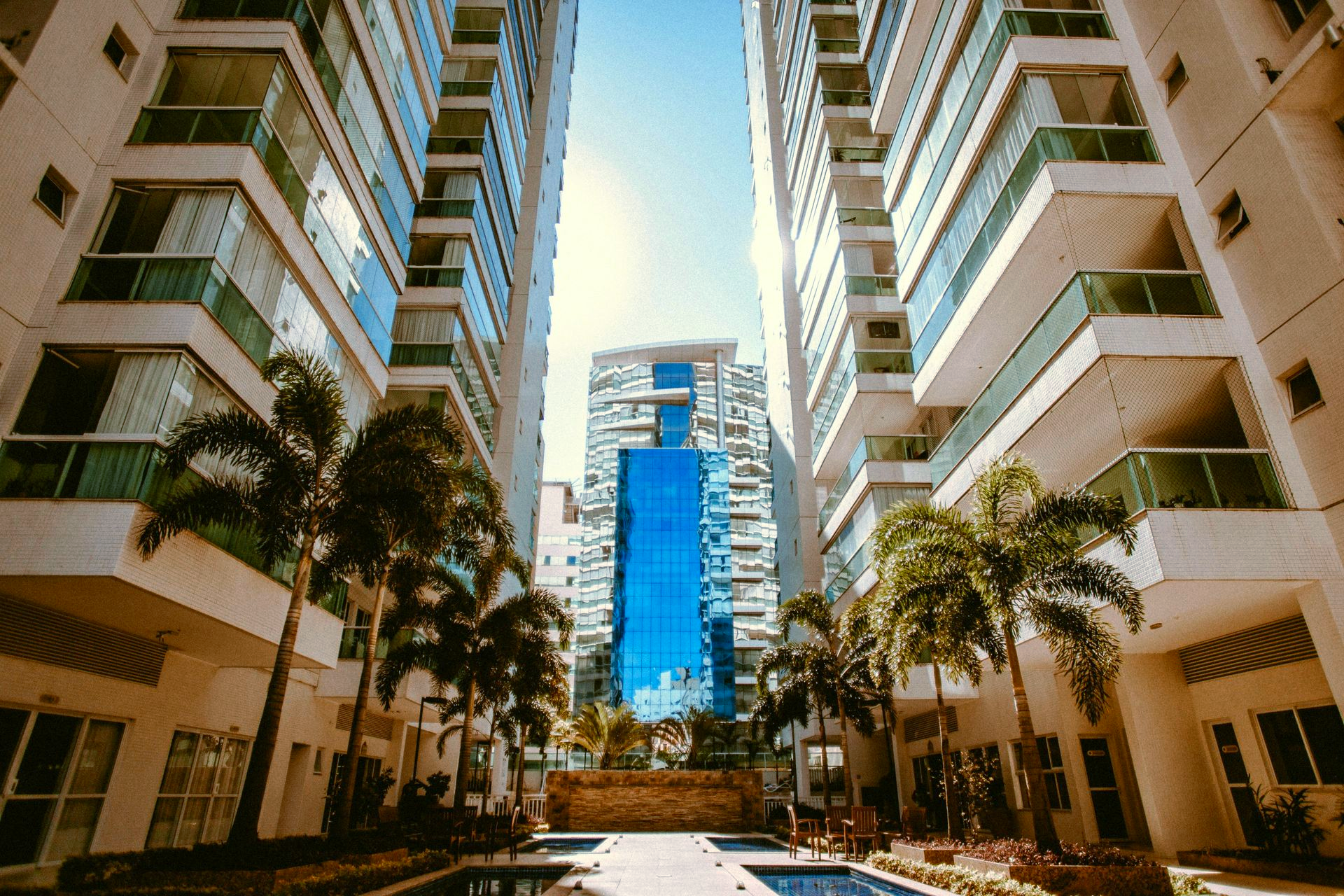 Modern apartment courtyard with palm trees and a blue glass tower in the background