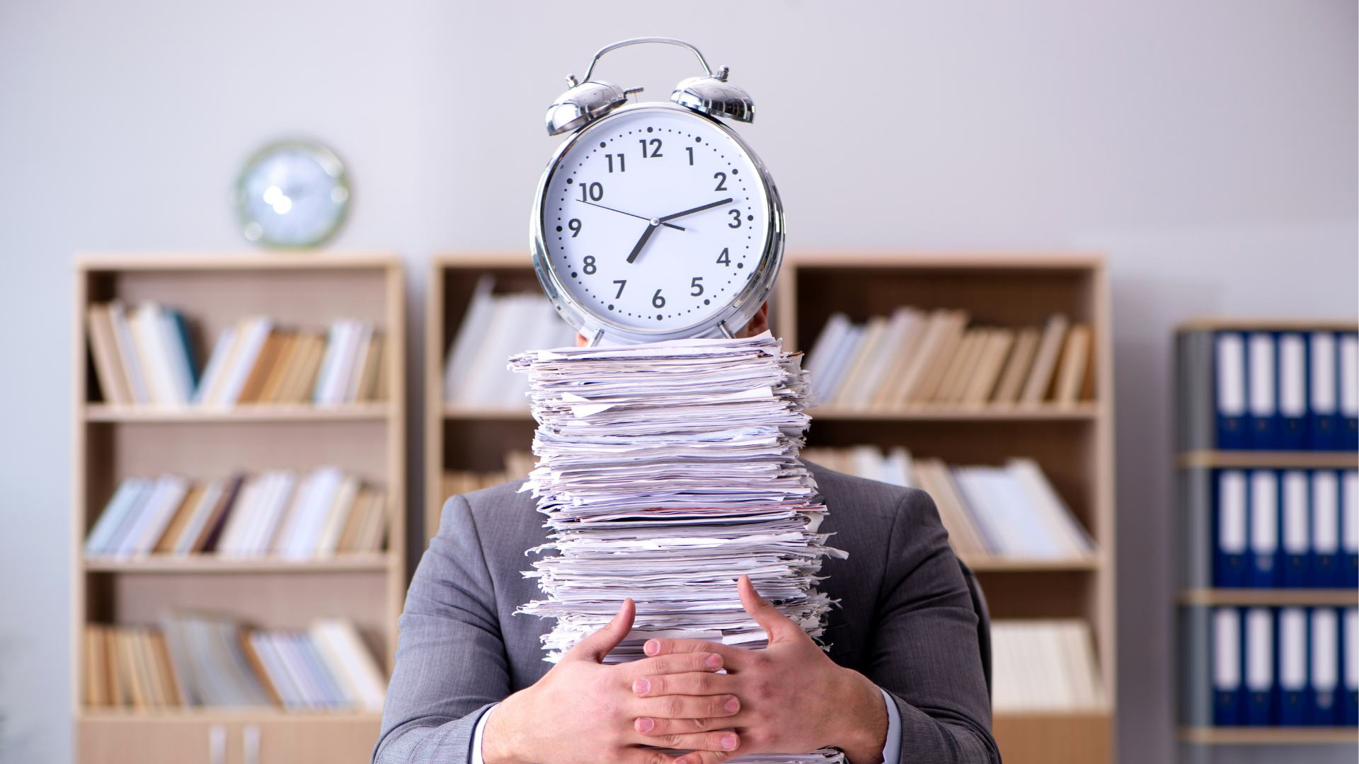 Stressed person buried in paperwork with an alarm clock on their head in an office