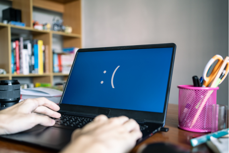 Person using a laptop with a blue sad face on the screen in a home office