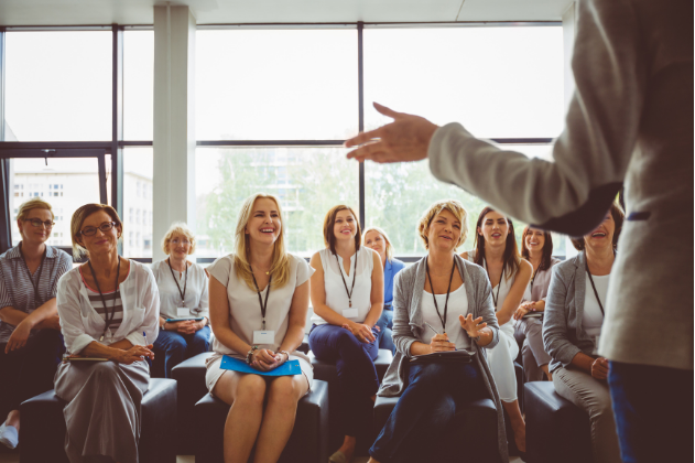 Speaker addressing a seated audience in a bright meeting room