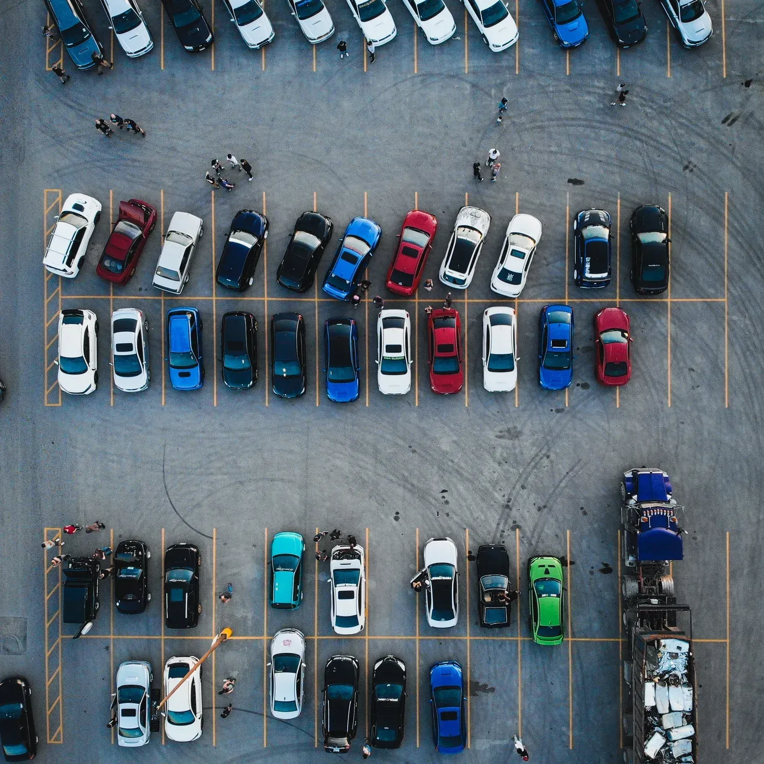 Aerial view of a parking lot with rows of parked cars in various colors, including blue, white, black, and red.