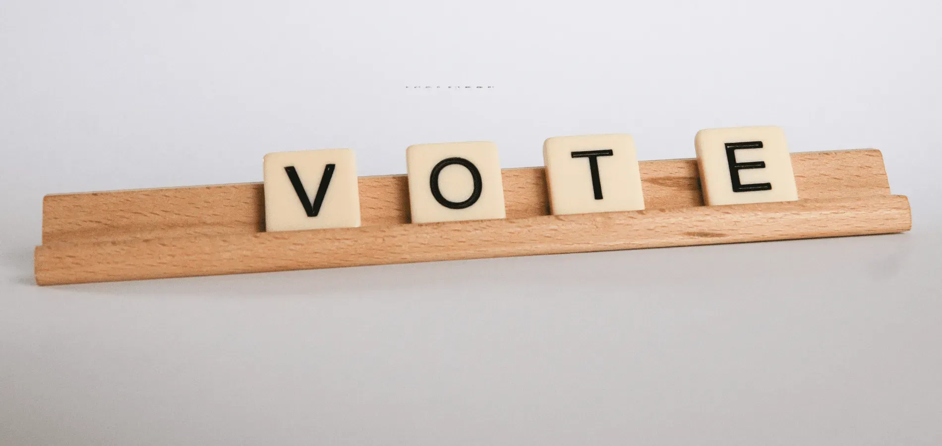 Wooden letter tiles spelling VOTE on a tile rack, illustrating condominium board election ballots