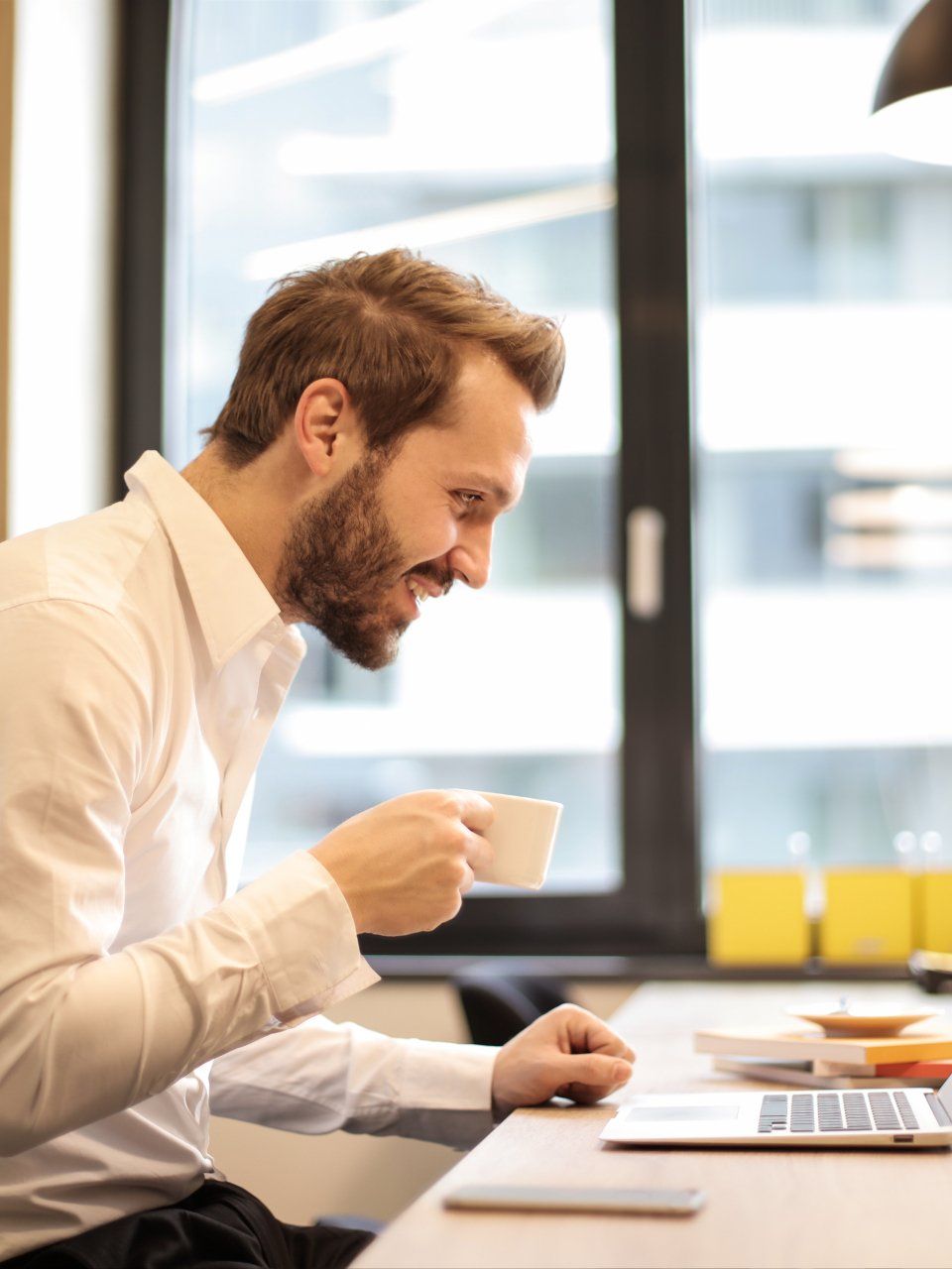 een man drinkt koffie terwijl hij een laptopcomputer gebruikt.