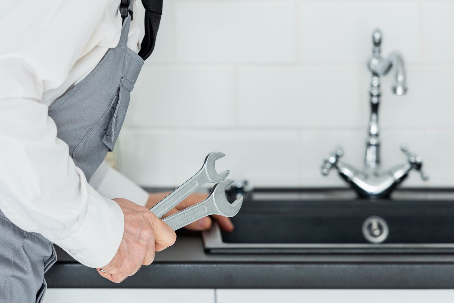 Plumber tightening a faucet under a kitchen sink with a wrench