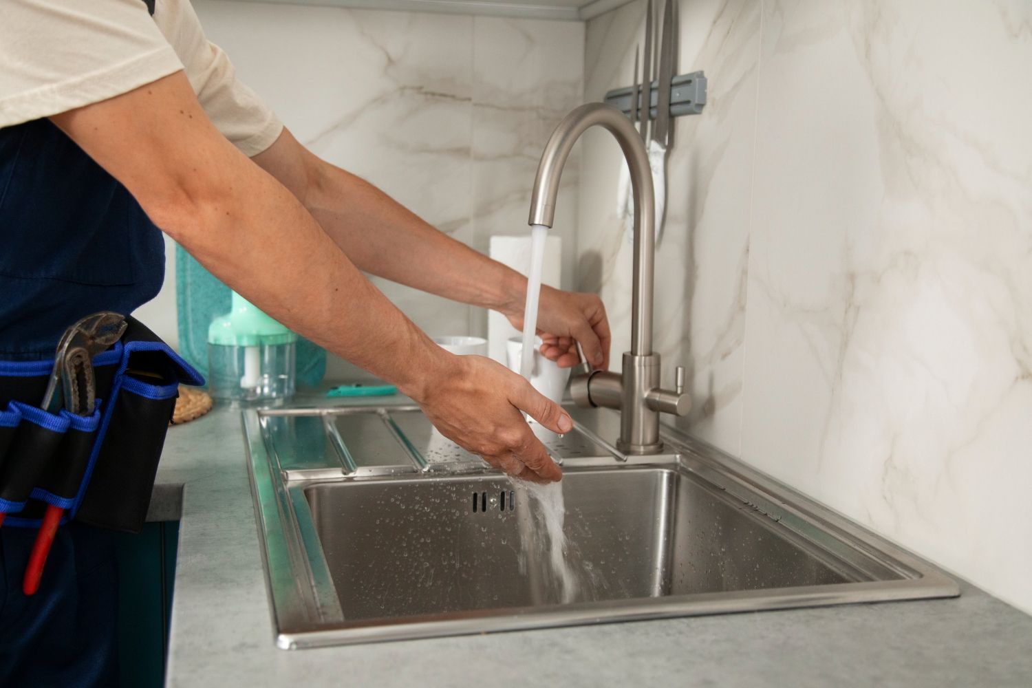 Person washing hands at a stainless steel kitchen sink under running water