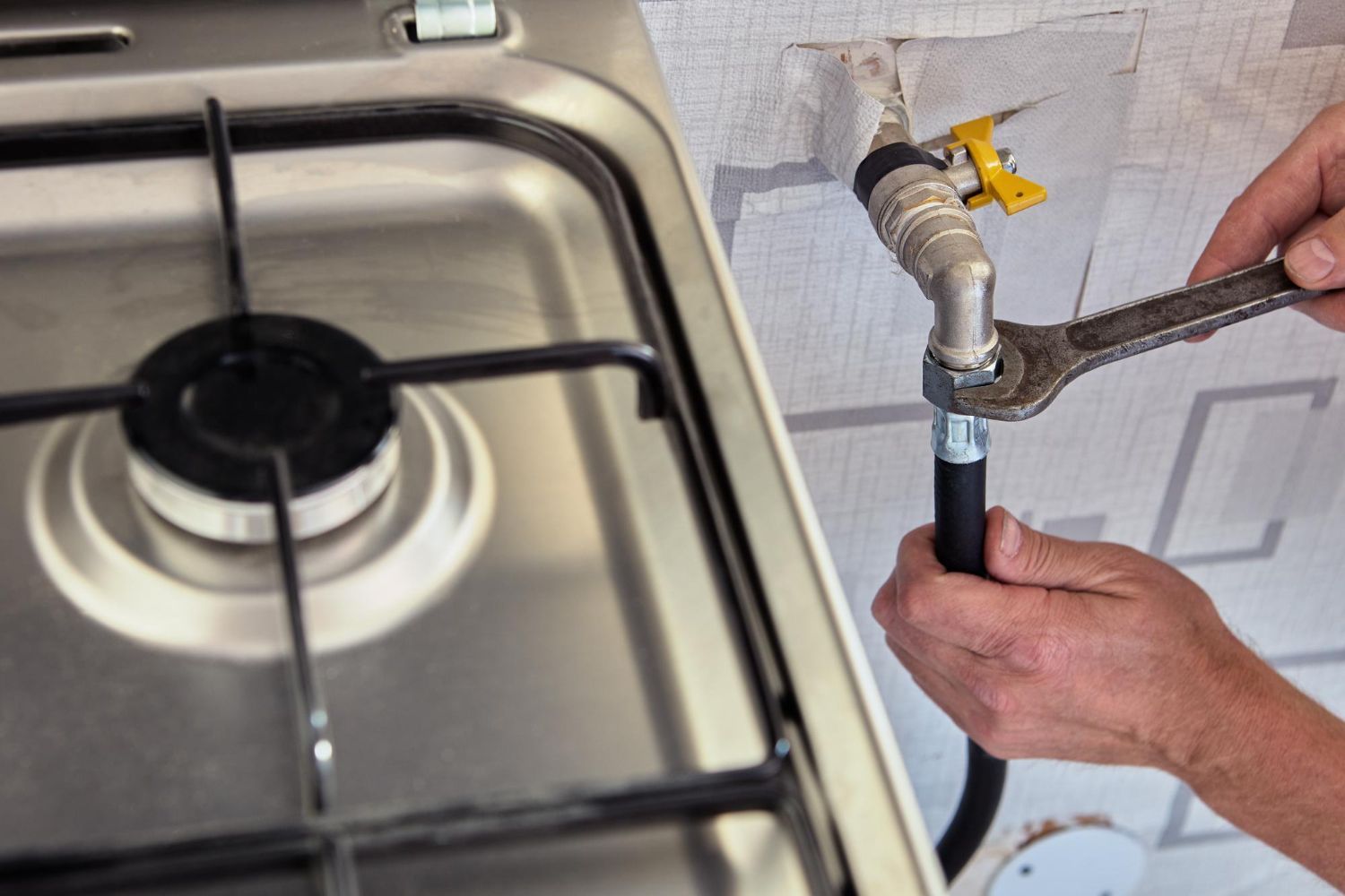 Hands using a wrench to tighten a gas pipe next to a stovetop