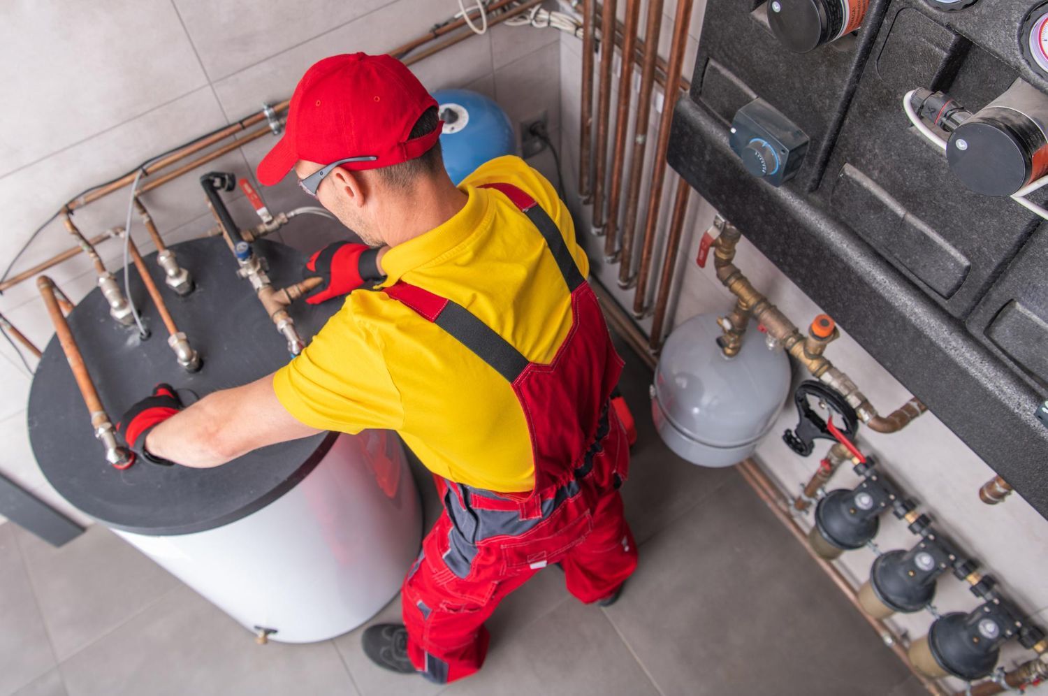 Plumber in red overalls working on water heaters in a utility room