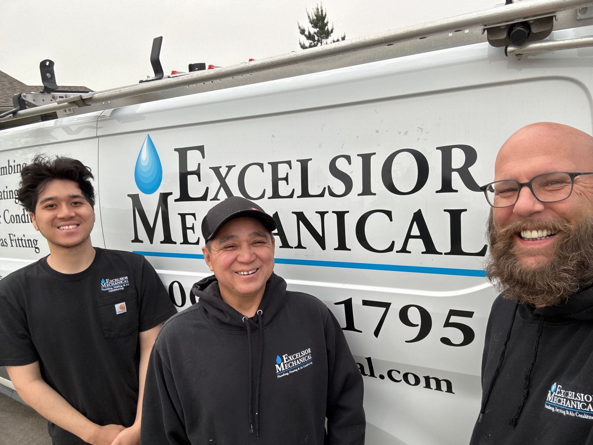 Three men are standing in front of a van that says excelsior mechanical.