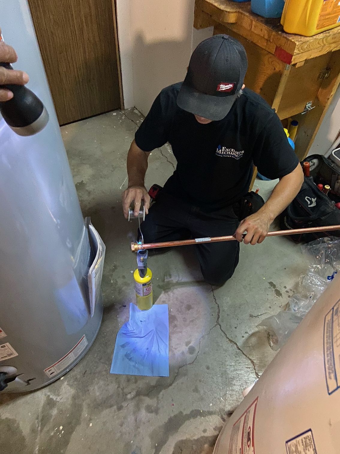 A man is working on a water heater in a basement.
