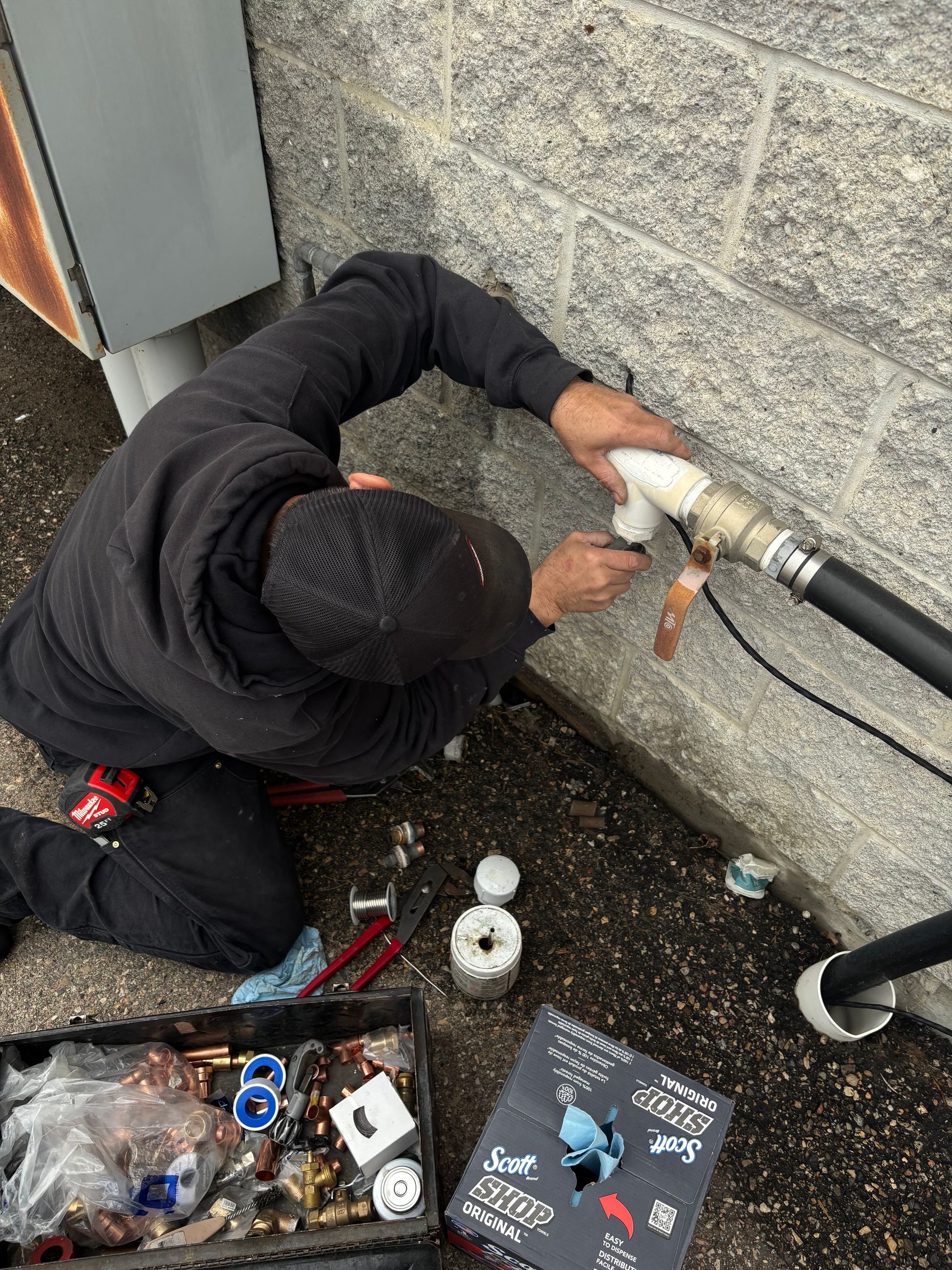 A man is working on a pipe outside of a building.