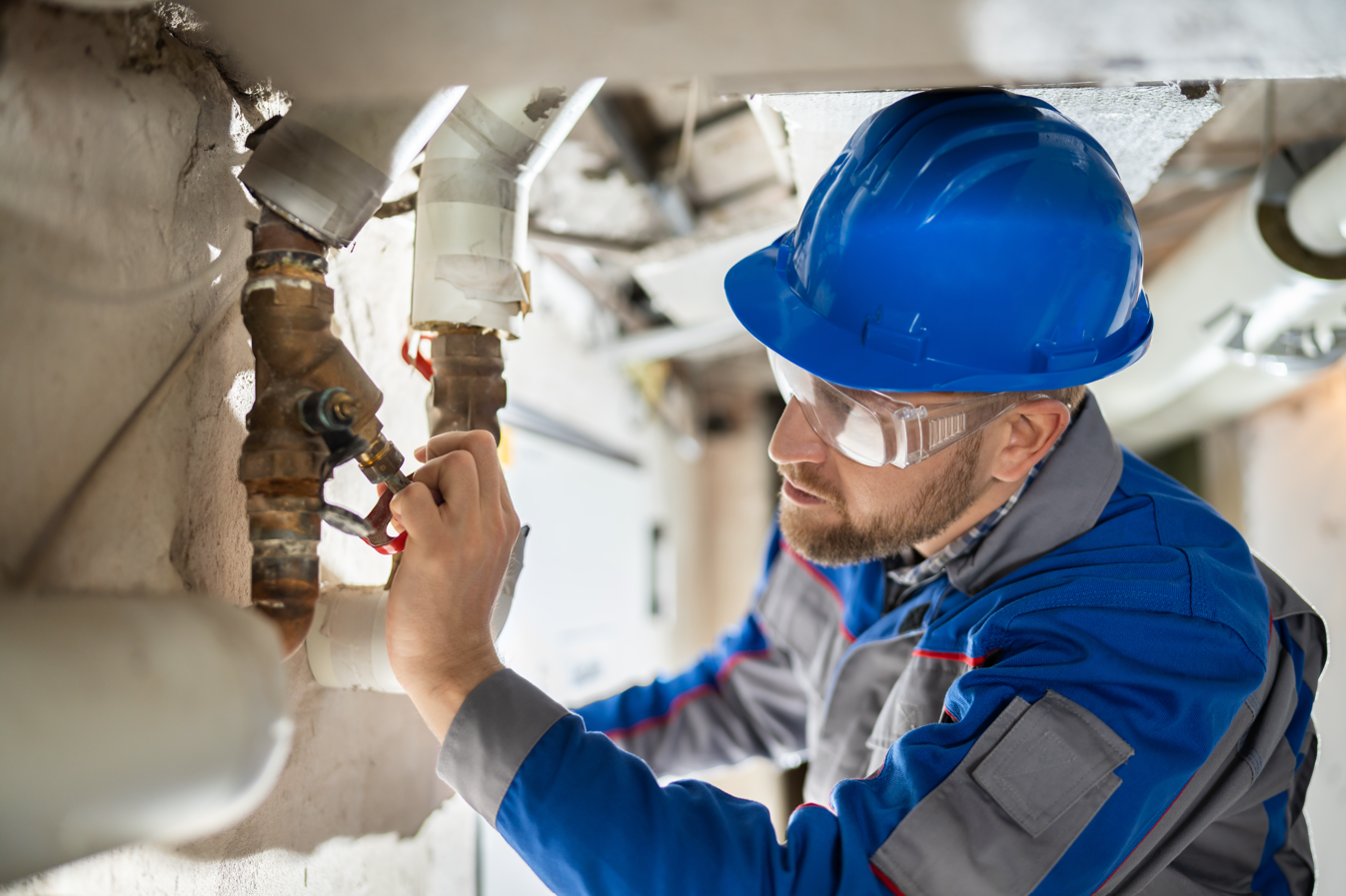 a man wearing a hard hat and safety glasses is working on a pipe .