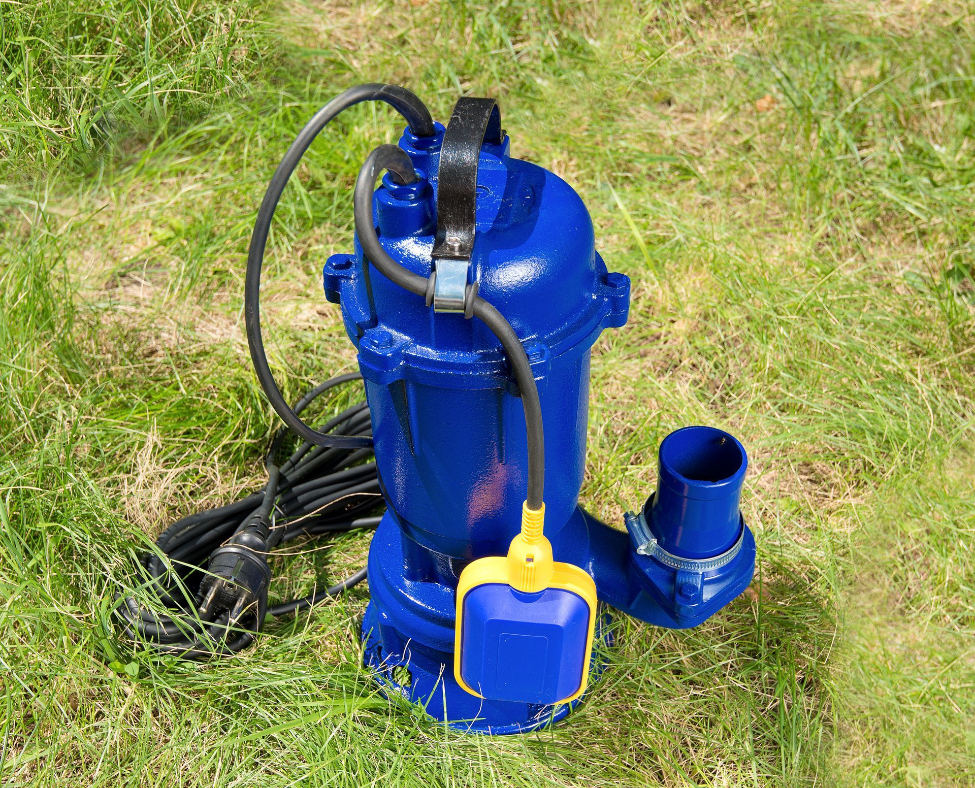 Blue submersible water pump with hoses on grass outdoors