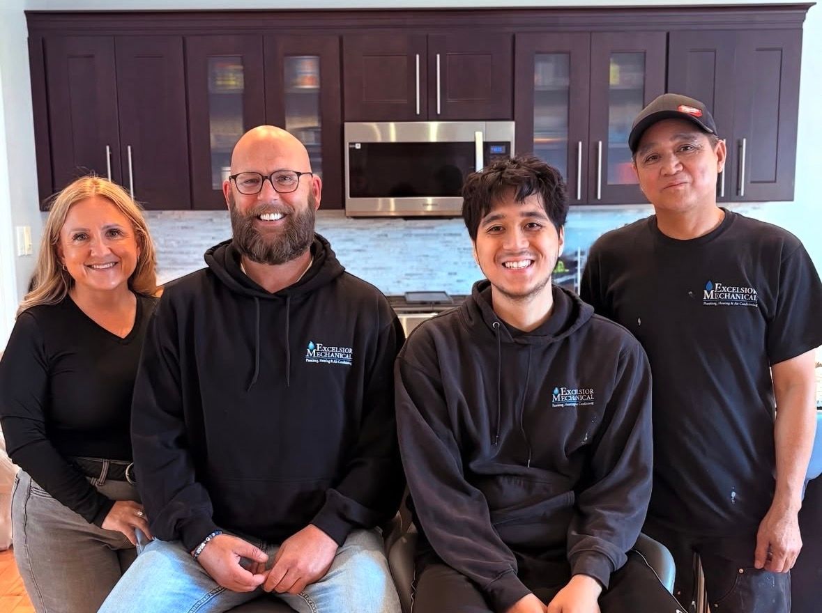 Four people in black shirts posing in a kitchen with dark cabinets and stainless steel appliances.