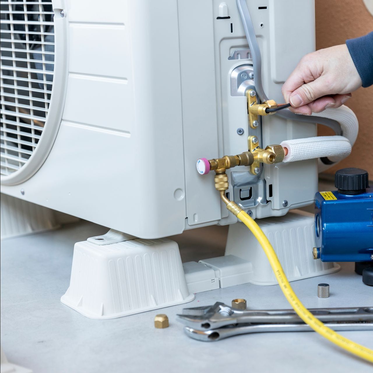 A person is fixing an air conditioner with a vacuum pump