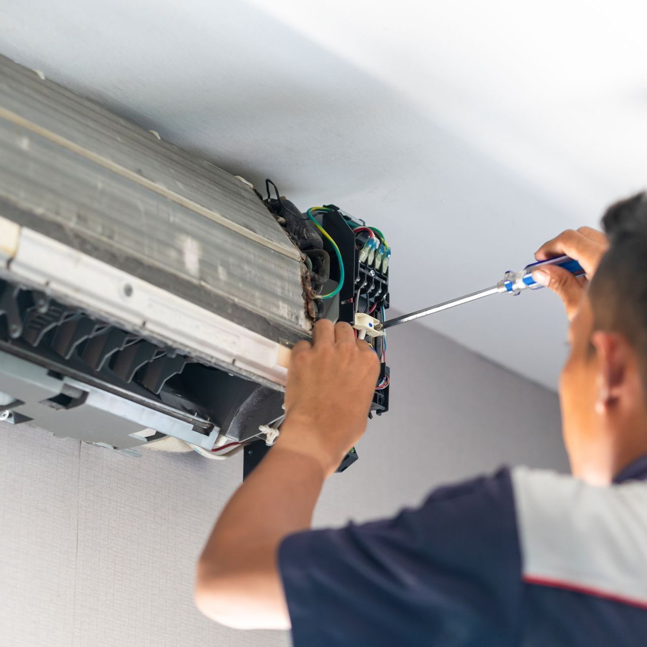A man is fixing an air conditioner with a screwdriver.