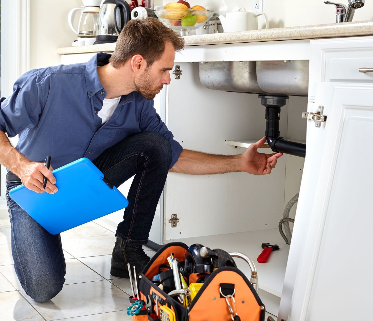 a man is kneeling down in a kitchen looking under a sink .