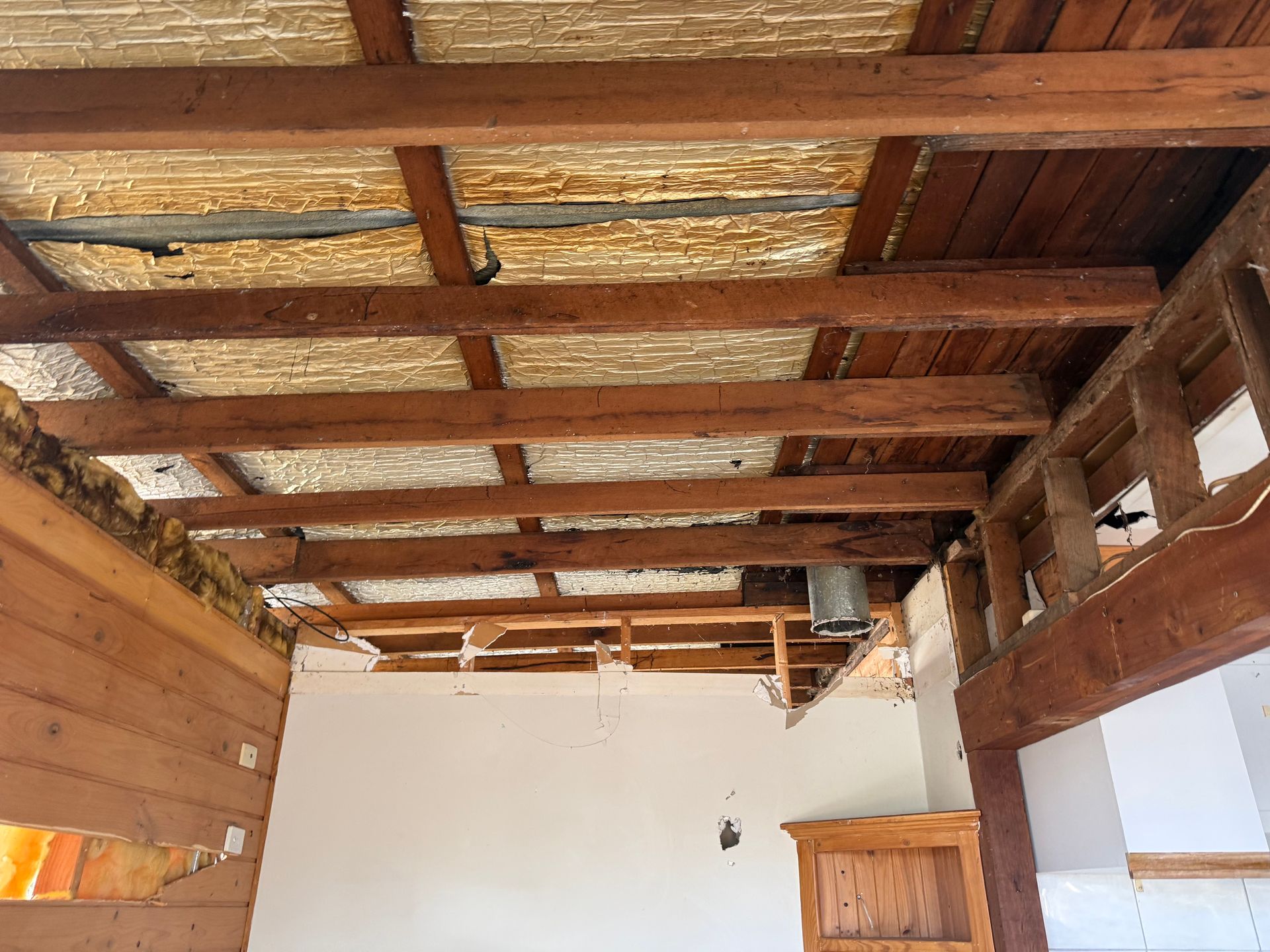 Exposed wooden ceiling beams in a rustic room with white walls and a wooden cabinet.