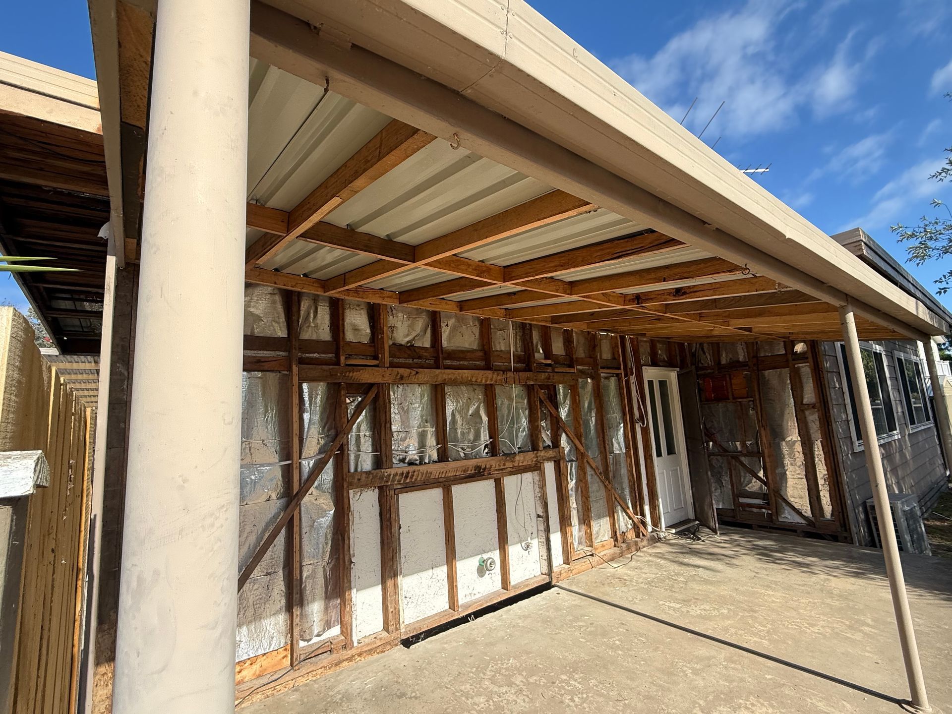 Weathered backyard shed with rusted metal walls and a covered patio under a blue sky
