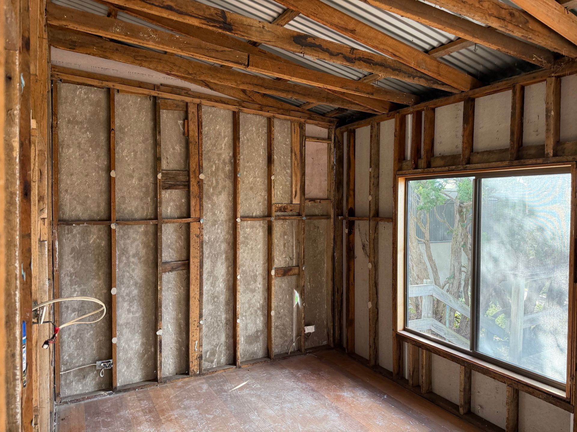 Empty room under construction with exposed wooden framing and a large window on the right.