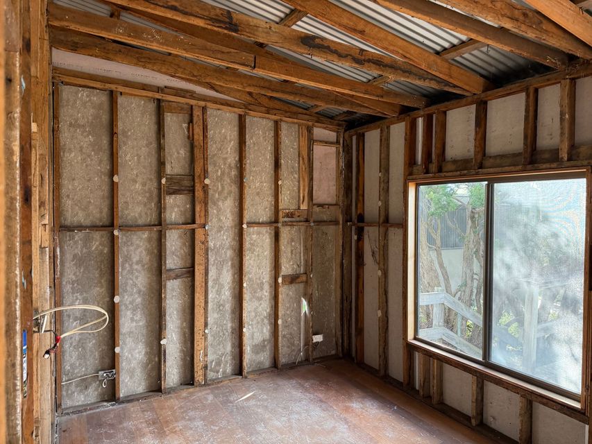 Unfinished room with exposed wooden studs, insulation, and a large window letting in daylight.