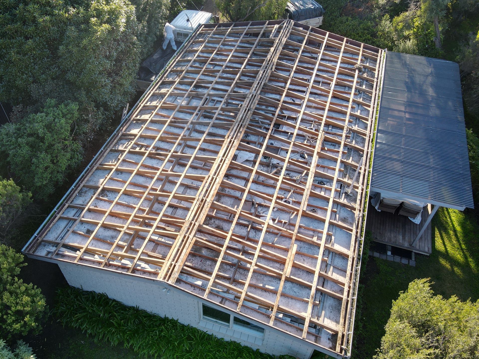 Aerial view of a house roof under repair, with exposed wooden rafters and a corrugated metal section.