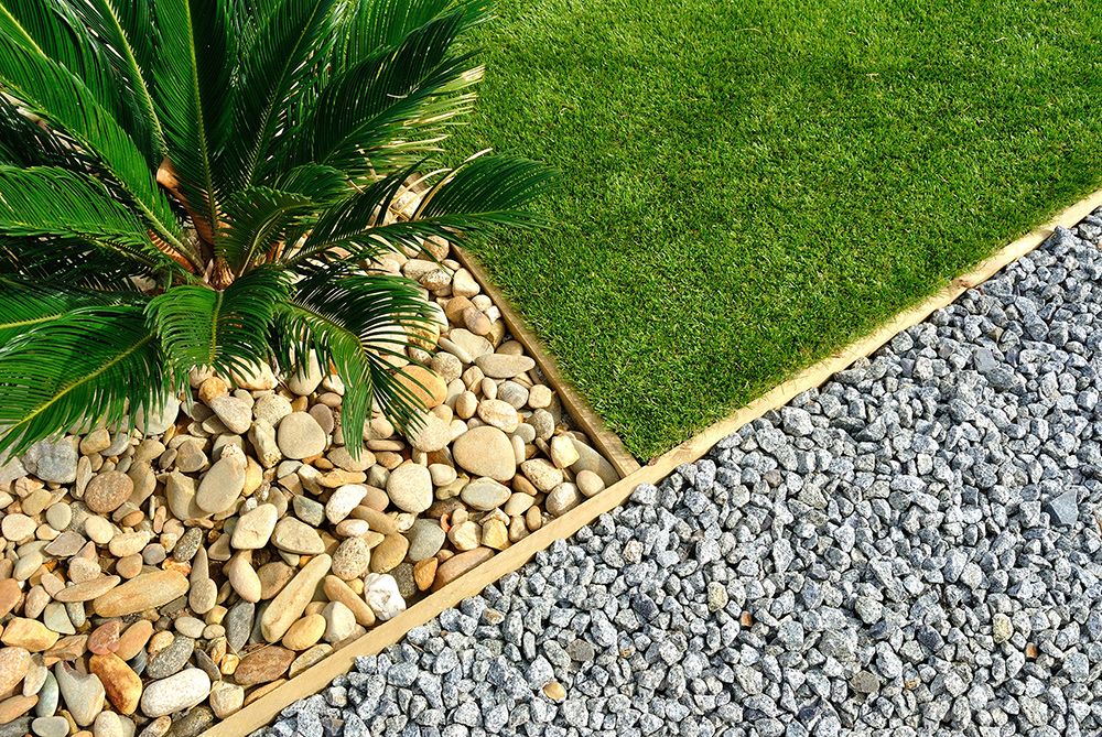 A landscaped garden bed with a Cycas palm, pebbles, gravel, and artificial grass bordered by wood.