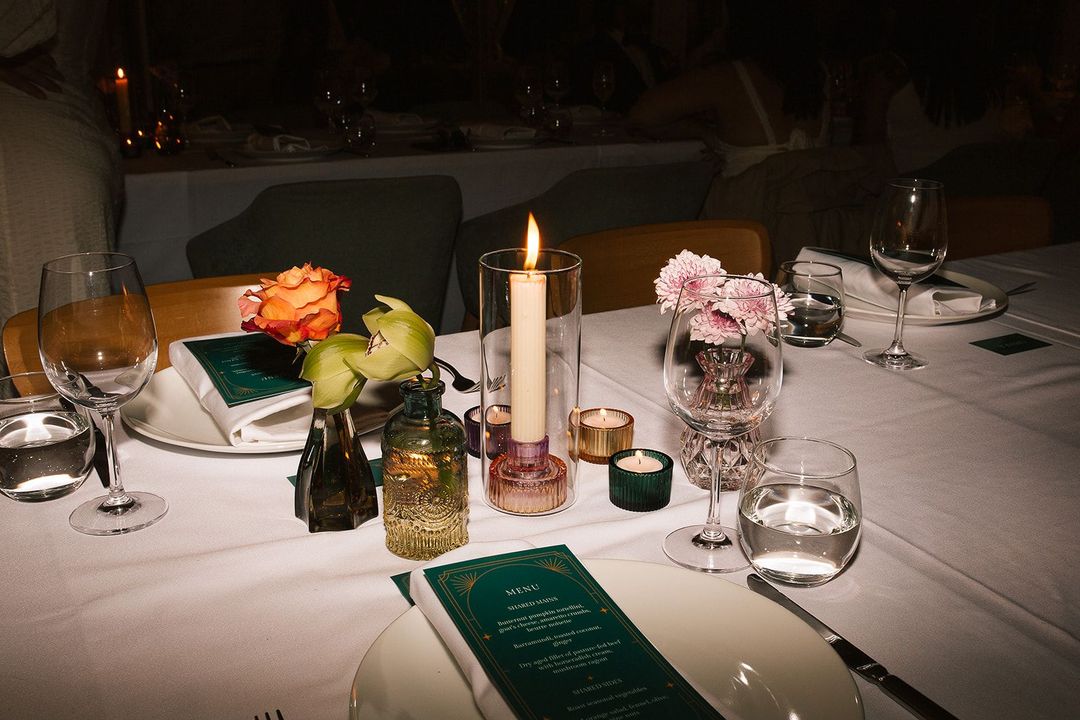 Elegant dining table set with flowers, candles, glassware, and menus.
