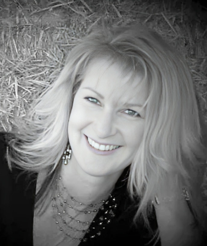 A woman is smiling in front of a pile of hay