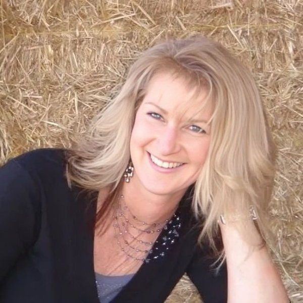 A woman is smiling in front of a pile of hay