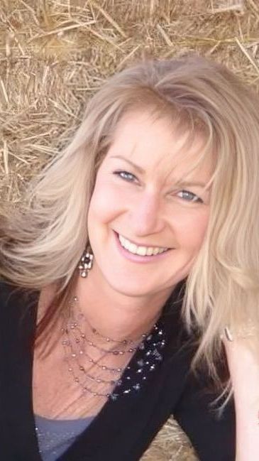 A woman is smiling in front of a pile of hay.