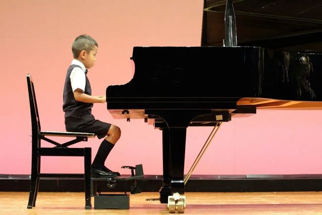 A young boy is sitting in a chair playing a piano