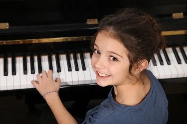 A young girl is smiling while playing a piano