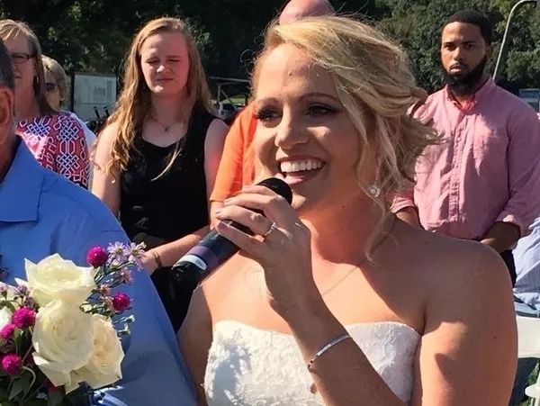 A woman in a wedding dress is holding a microphone and smiling.